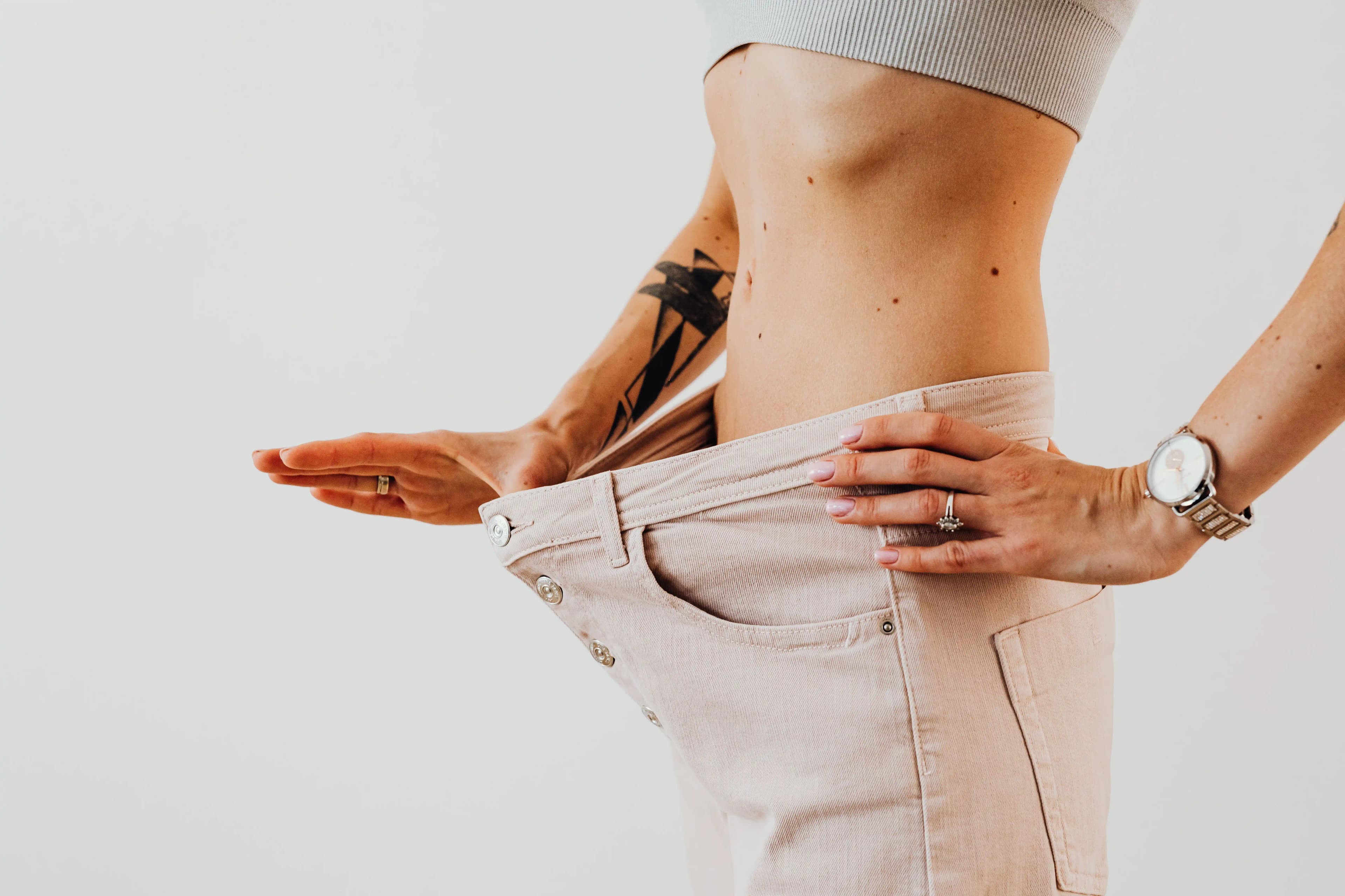 ilustrasi seorang wanita dengan celana longgar yang menunjukkan kemajuan penurunan berat badan